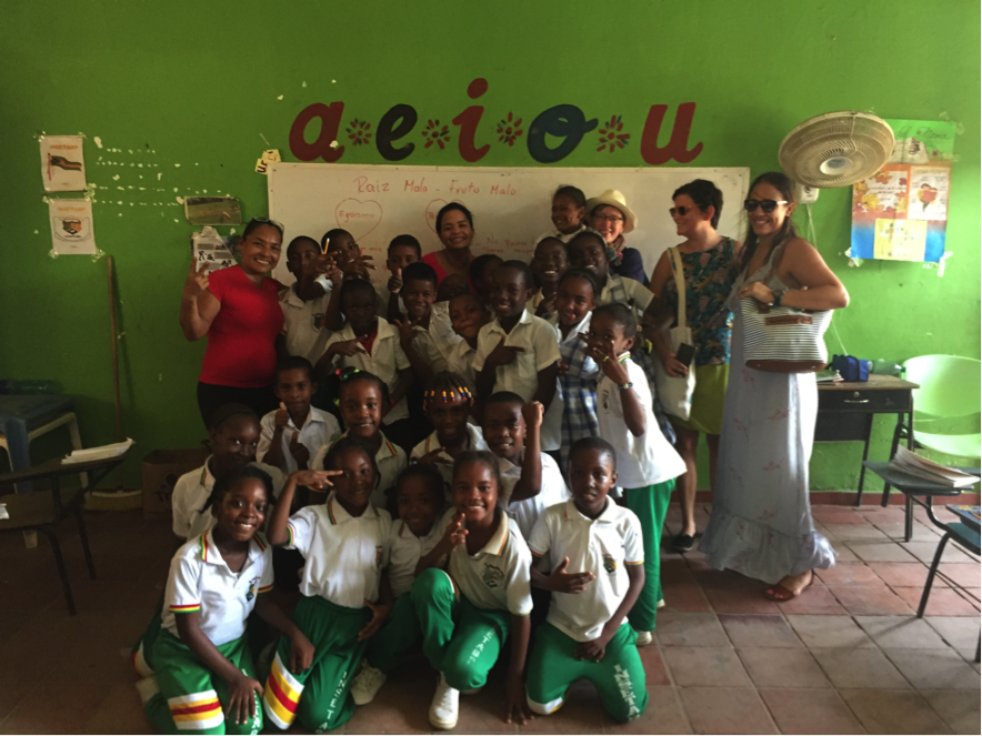 Photograph showing several children in uniform, teachers and visitors posing in a classroom, laughing and smiling