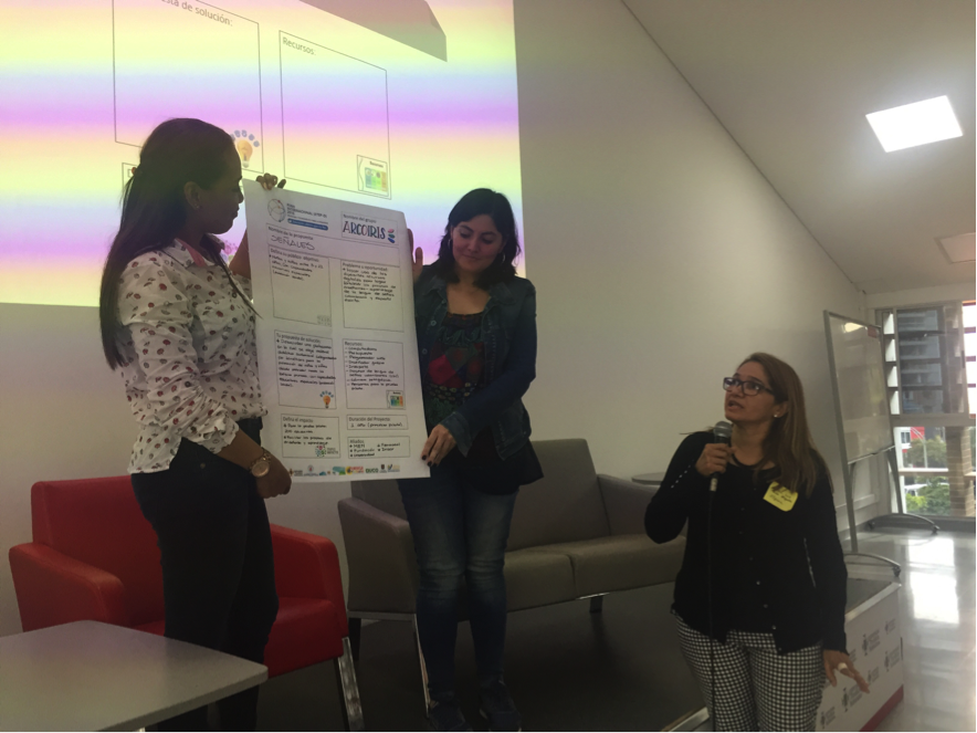 Photograph showing 2 participants holding up a poster while a third participant speaks into a microphone